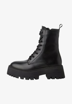 Bottines noires en cuir avec lacets, dotées d'une semelle en caoutchouc noire épaisse, d'un col rembourré et d'une languette pour un enfilage facile. Texture lisse.