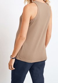 Haut sans manches beige avec un col arrondi, en tissu coton lisse et une coupe décontractée, assorti à un pantalon bleu foncé.