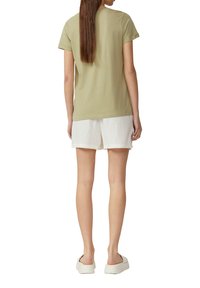 Olijfgroen katoenen t-shirt met korte mouwen, gecombineerd met witte linnen shorts. De achterkant heeft een afgeronde zoom en minimale ontwerpdetaillering.