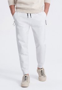 Witte joggerbroeken met zwarte trekkoorden, gemaakt van structuurstof en met zijritszakken. Gecombineerd met beige sneakers, wat een casual look laat zien.