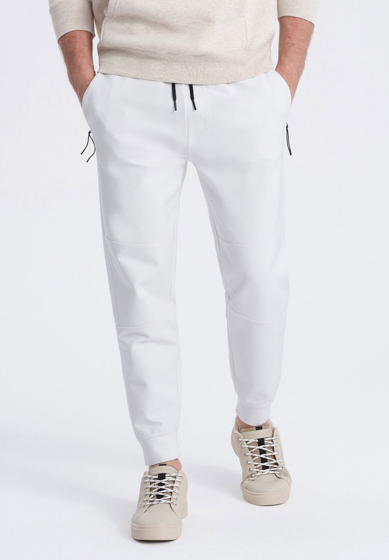 Witte joggerbroeken met zwarte trekkoorden, gemaakt van structuurstof en met zijritszakken. Gecombineerd met beige sneakers, wat een casual look laat zien.