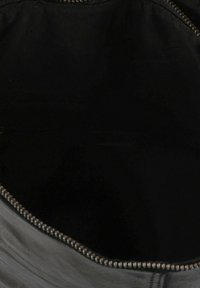 Interior de bolso de cuero negro con textura suave; cuenta con cremallera metálica a lo largo del borde; diseño oscuro y minimalista sin patrones visibles.