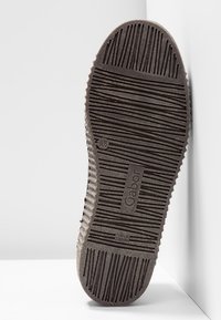 Semelle de chaussure avec rainures diagonales et verticales texturées, logo "Gabor" embossé au centre, positionnée debout contre un coin blanc.