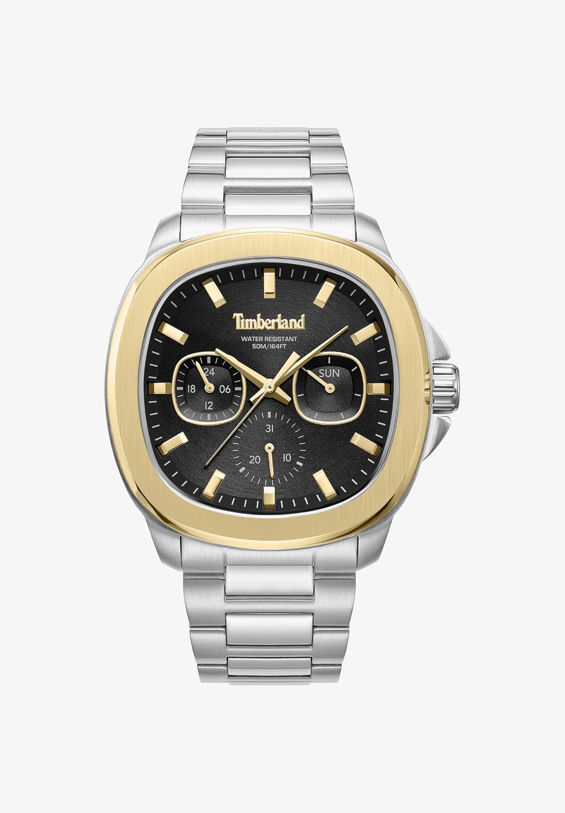 Neliön muotoinen kello mustalla kellotaululla, kultaisilla yksityiskohtilla ja hopeisella ruostumattomasta teräksestä valmistetulla rannekkeella. Ominaisuuksiin kuuluvat päivämäärä- ja viikkonäytöt sekä hohtavat tuntimerkit.