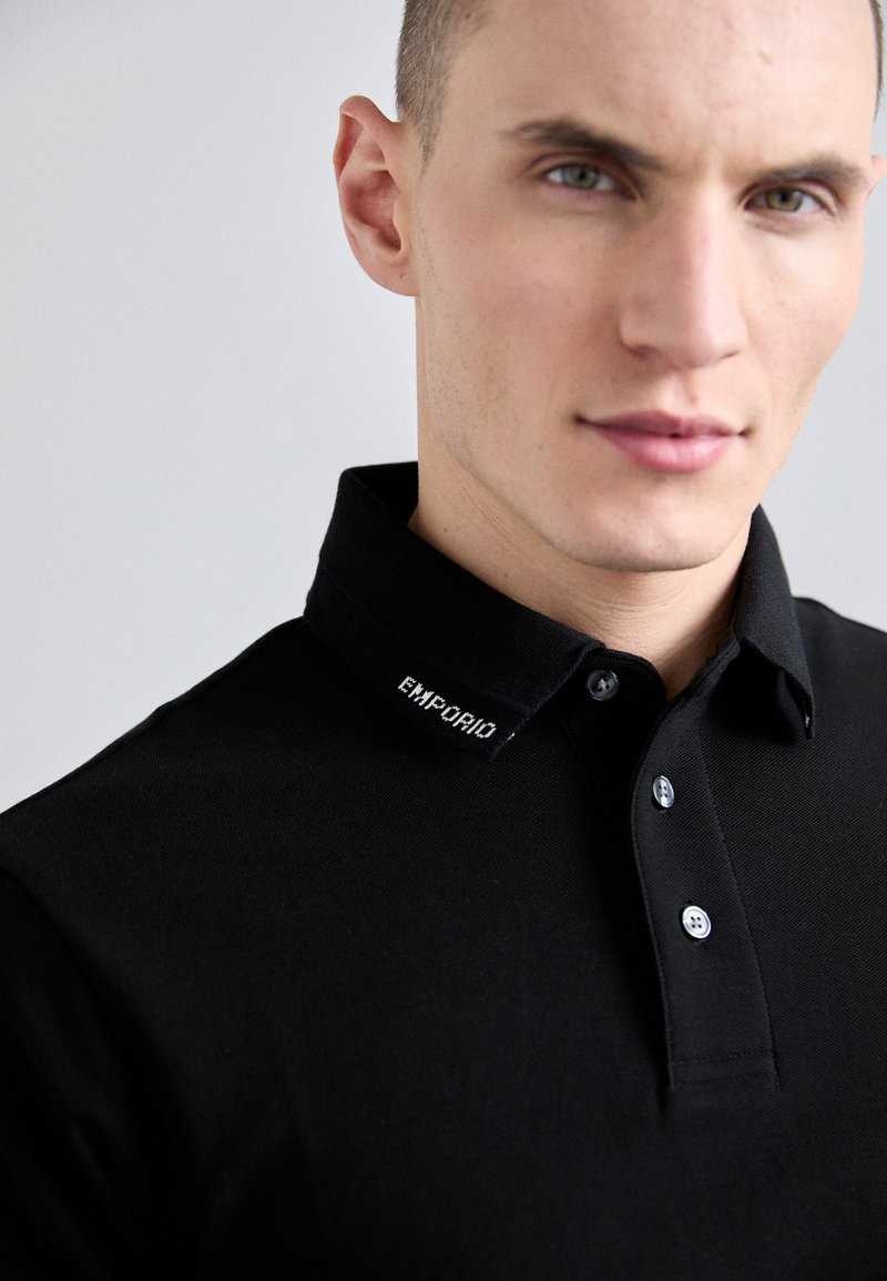 Black polo shirt featuring a classic collar, a subtle logo embroidered on the collar, and a button-down design with two buttons.