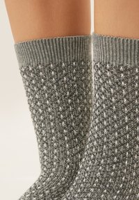 Gray knitted socks with textured pattern and metallic thread accents, featuring ribbed cuffs for a snug fit.
