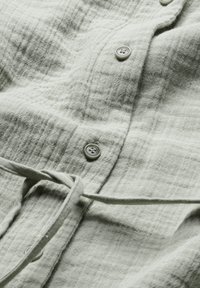 Camicia button-up verde chiaro realizzata in un tessuto testurizzato con un motivo a griglia sottile, dotata di coulisse e bottoni in plastica.