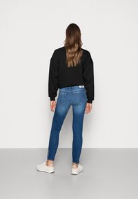 Svart sweatshirt, blå tajta jeans med bakfickor och vita sneakers. Outfiten har en avslappnad passform och en mjuk tygtextur.