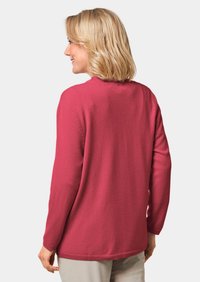 Lange mouwtrui in een levendige roze kleur, met een ronde halslijn en een gebreide textuur, gedragen over lichte broek.