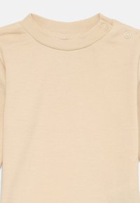 Vaaleanbeige pitkähihaisuus vauvan bodysuit, jossa on pyöreä pääntie ja kaksi nepparia olkapäällä, jotta pukeutuminen on helppoa.