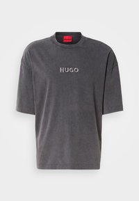 Graues, lässiges T-Shirt mit kurzen Ärmeln, runder Ausschnitt, mit einem gestickten "HUGO"-Logo in einem helleren Farbton auf der Vorderseite, aus weichem Stoff mit einer glatten Textur.