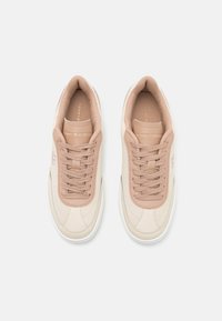 Baskets beige clair avec une texture lisse, dotées d'un design perforé, de lacets assortis et d'un détail de logo subtil sur le côté.
