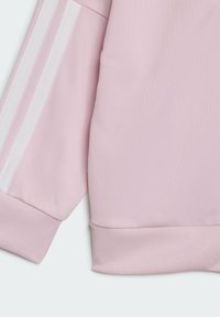 Rosa sweatshirtärm med ribbade muddar, prydd med två vita ränder längs längden. Tyget har en texturerad yta för hållbarhet.