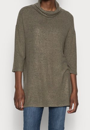 Top en tricot vert olive avec un col drapé, des manches trois-quarts et une coupe décontractée, associé à un jean bleu clair.