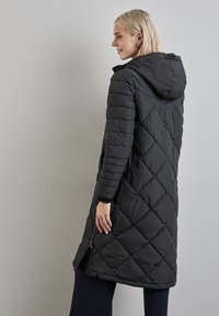 Černá péřová bunda s kapucí, s diamantovým prošíváním, předním zipem a bočními kapsami. Hladký povrch, střední délka.