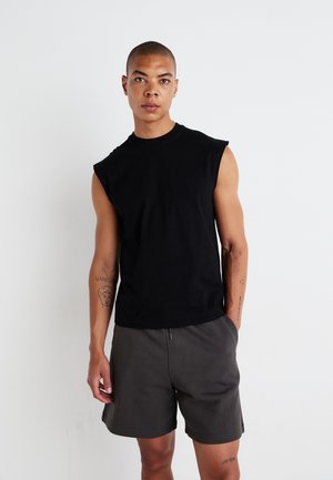Schwarzes ärmelloses T-Shirt aus Baumwolle mit Rundhalsausschnitt und lockerer Passform, kombiniert mit dunkelgrauen Shorts mit Seitentaschen.
