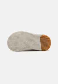 Semelle de chaussure avec une base en caoutchouc blanc et des rainures horizontales pour l'adhérence, et un accent texturé brun au niveau du talon.