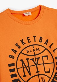 Sudadera de algodón naranja con cuello redondo. Presenta impresiones gráficas en negro que dicen "BASKETBALL SLAM NYC" centradas en la parte frontal.