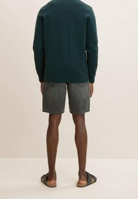 Maglione verde scuro, pantaloni corti in denim grigio e sandali neri. Il maglione ha un collo rotondo con una finitura texturizzata; i pantaloni corti sono fino al ginocchio con un effetto sbiadito.