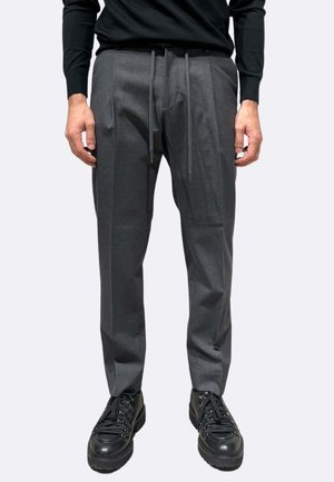 Pantaloni grigi su misura con finitura strutturata, vita elastica con coulisse, pieghe sul davanti, abbinati a sneakers nere chunky.