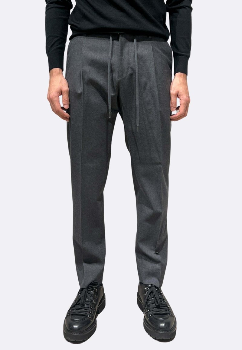 Pantaloni grigi su misura con finitura strutturata, vita elastica con coulisse, pieghe sul davanti, abbinati a sneakers nere chunky.