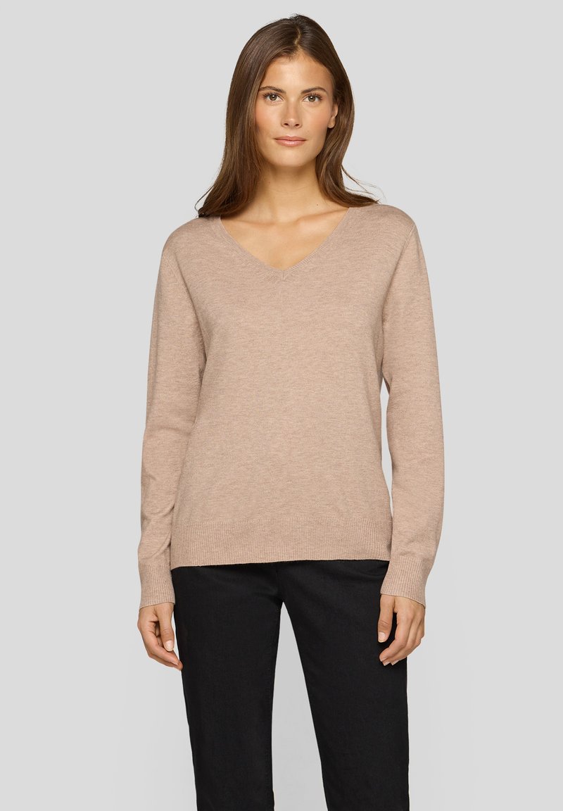 Beiger V-Ausschnitt-Pullover aus weichem Stoff, mit langen Ärmeln sowie gerippten Bündchen und Saum. Kombiniert mit schwarzen Hosen für einen kompletten Look.