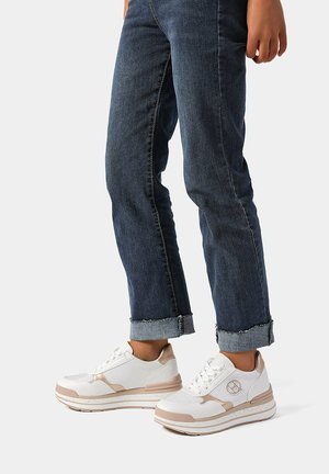 Scarpe da ginnastica bianche e beige realizzate in materiali a rete e sintetici, con supporto per la caviglia imbottito e suole testurizzate. Indossate con jeans di denim risvoltati.