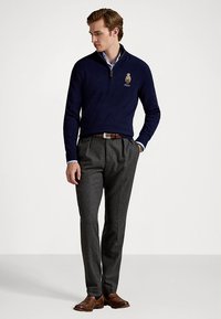 Μπλε ζακέτα με φερμουάρ και κεντημένο λογότυπο, συνδυασμένη με γκρι, σε στενή γραμμή, παντελόνια και καφέ δερμάτινα παπούτσια. Υφασμάτινη υφή και εφαρμοστή σχεδίαση.