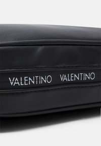 Svart läderväska med präglade "VALENTINO"-logotyper, elegant design, slät textur och distinkta sömmar längs kanterna.