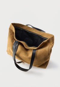 Καφέ σουέτ τσάντα ώμου με μαύρες δερμάτινες λαβές, ανοιχτό πάνω μέρος που αποκαλύπτει εσωτερικό από μαύρο ύφασμα και εσωτερική τσέπη με φερμουάρ.