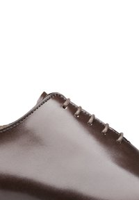 Chaussure en cuir marron avec une finition lisse, présentant un bout arrondi et des lacets gris sur le dessus. Design épuré avec de fines coutures.