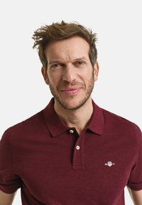 Bordeaux polo shirt van een gestructureerde stof, met korte mouwen en een knoopsluiting met twee knopen. Bevat een klein logo op de borst.