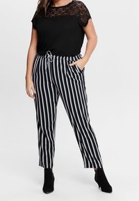 Svart topp med spetsoverdrag, kombinerad med svart- och vitrandiga byxor med elastisk midja och knytning. Svarta ankelboots fulländar looken.