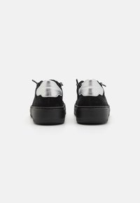 Czarne zamszowe sneakersy z teksturowanym srebrnym skórzanym akcentem na pięcie, z zaokrąglonymi krawędziami i grubą czarną gumową podeszwą.