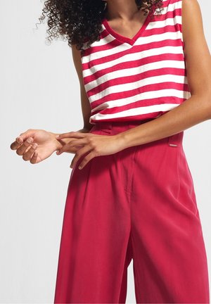 Paskowana, czerwona i biała, bezrękawnik z dekoltem w kształcie litery V, w połączeniu z wysokim stanem czerwonych spodni z subtelnym przeszyciem z przodu i bocznymi kieszeniami.