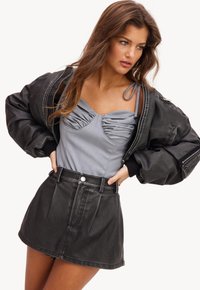 Zwarte bomberjack met oversized mouwen, gecombineerd met een grijze gerimpelde top en een hoge zwarte denim minirok. Gladde leren textuur.