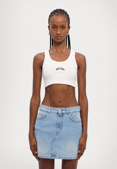Biela rebrovaná crop top s logom "GCDS"; skombinovaná s modrou džínovou mini sukňou so zapínaním na gombíky vpredu a vreckami, hladká textúra.