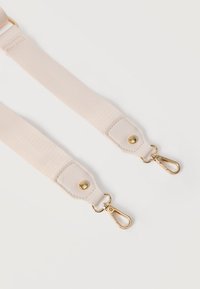 Deux sangles de sac en tissu beige avec des mousquetons pivotants dorés et des renforts en cuir cousu sur fond blanc.