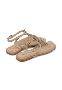 Sandali piatti beige con finitura scamosciata, caratterizzati da strass decorativi e cinturini alla caviglia regolabili. Punta quadrata e suola texturizzata.
