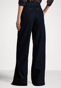 Vidbente mørke denimjeans med høyt liv, med baklommer og kontrasterende oransje søm langs sømmene og kanten.