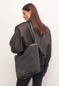 Szara skórzana torebka o zdefiniowanym kształcie, z czarnym paskiem, złotymi akcentami na dole i gładką fakturą.