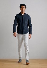 Granatowa koszula na guziki z długimi rękawami, zestawiona z białymi dopasowanymi spodniami i szarymi trampkami. Gładka tkanina z klasycznym kołnierzykiem.