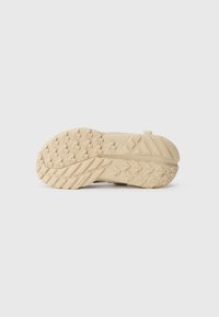 Suela de zapato deportivo en color beige claro con un patrón de superficie texturizada para mayor agarre, con surcos para flexibilidad y una sección de talón reforzada.