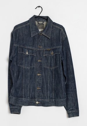 Veste en denim bleu foncé avec boutons sur le devant, deux poches poitrine avec boutons et un col ouvert, accrochée à un cintre noir.