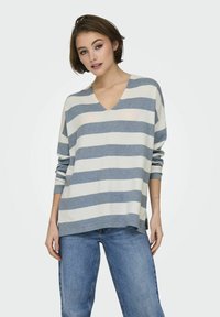 Maglione leggero a righe in grigio e crema, con scollo a V e vestibilità rilassata, maniche lunghe, abbinato a jeans blu.