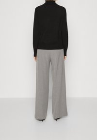 Maglione nero a collo alto abbinato a pantaloni larghi e leggeri grigi chiari. Il tessuto appare morbido con una consistenza liscia e dettagli minimi.