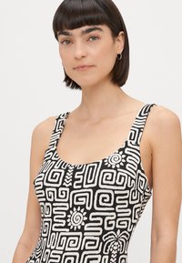Robe à motifs noir et blanc avec des designs géométriques, dotée de bretelles larges et d'un décolleté en scoop, fabriquée à partir d'un tissu texturé.