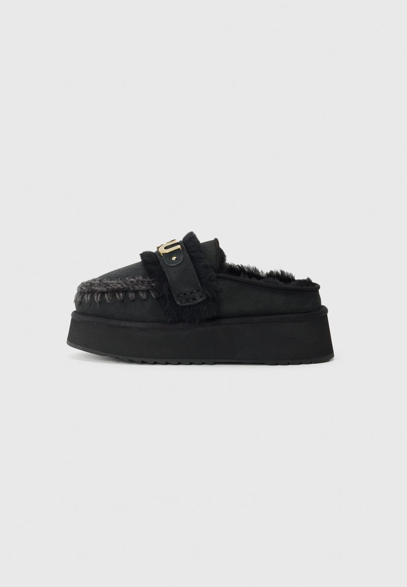 Čierne slip-on topánky s robustnou platformou, ktoré majú umelú kožušinu, pletené švy a zlatistý prackový detail na remienku.