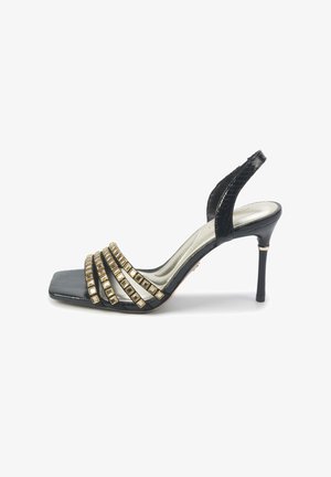 Zwarte hoge hak sandaal met een vierkante teen en drie banden versierd met gouden vierkante studs. Heeft een slanke, glanzende afwerking en een slanke hak.