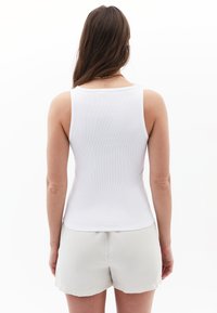 White ribbed tank top with wide straps, fitted design; worn with light gray shorts, smooth texture, simple and minimalistic style.